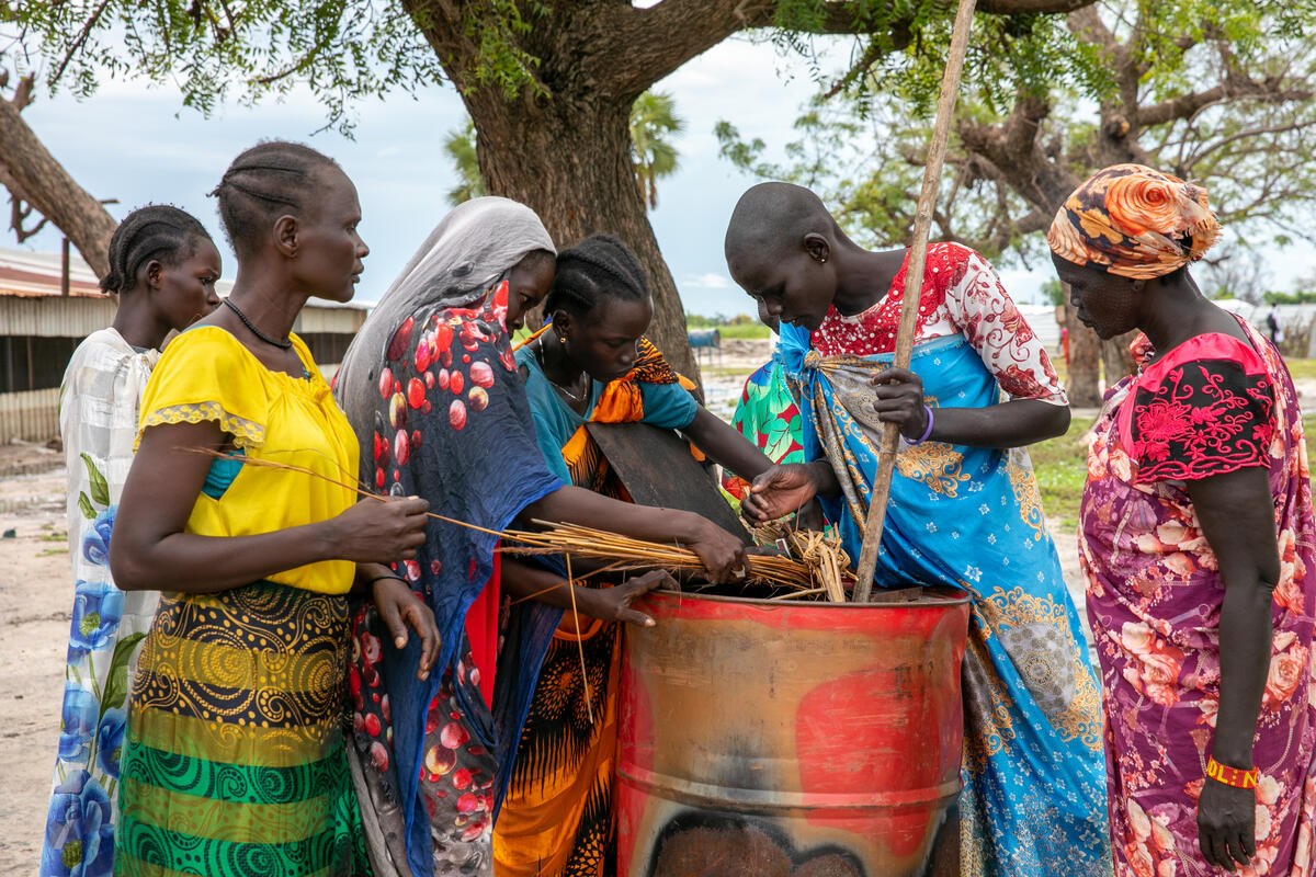 South Sudan. Women filling a metal oil barrel with dry water hyacinth.
