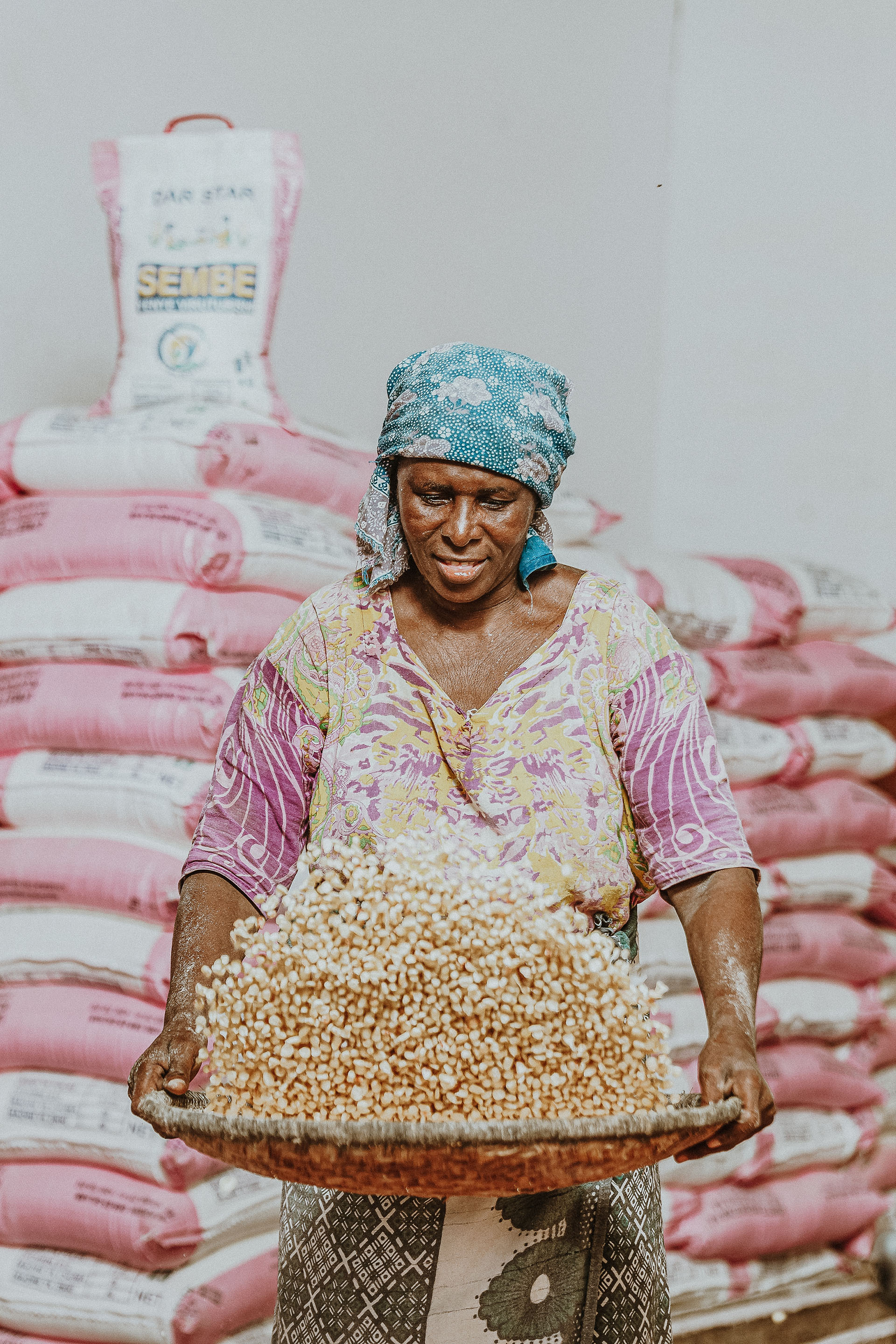Woman tosses a grain with bags of grains behind her.