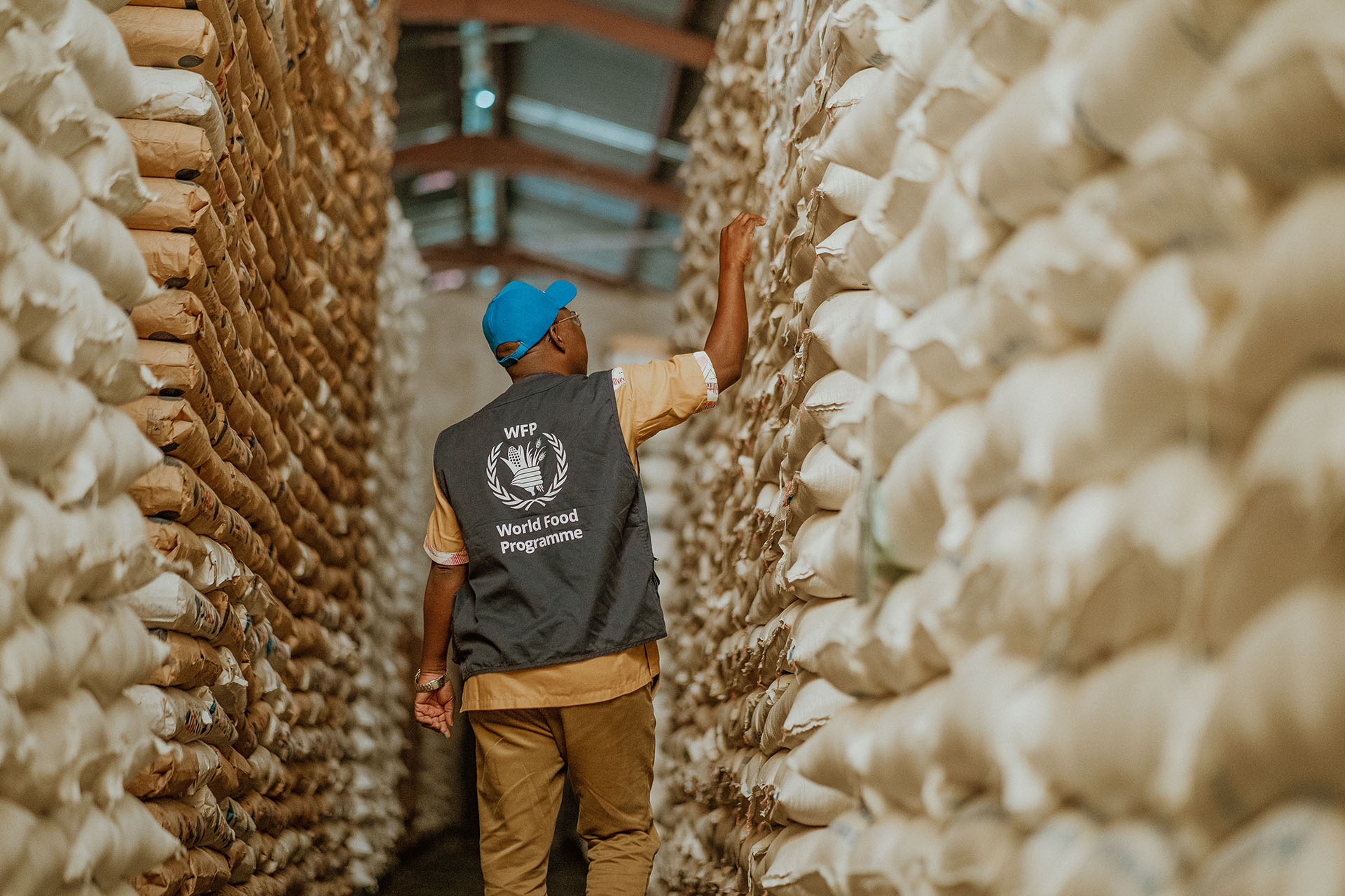 WFP Supply Chain staff walks through row of food parcels.