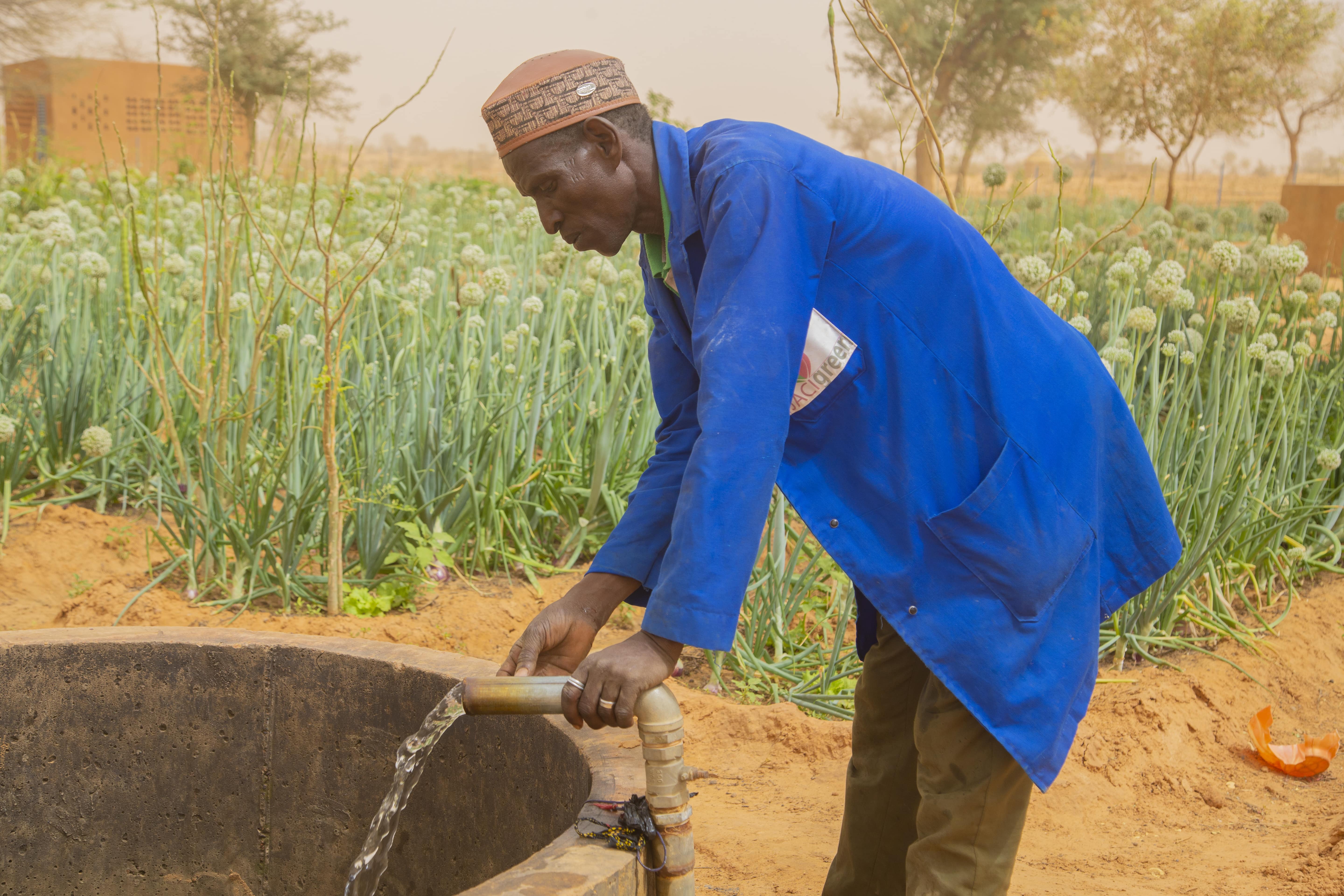 A man accesses water via a well pipe in a field.