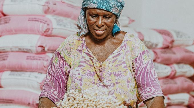 Woman tosses a grain with bags of grains behind her.