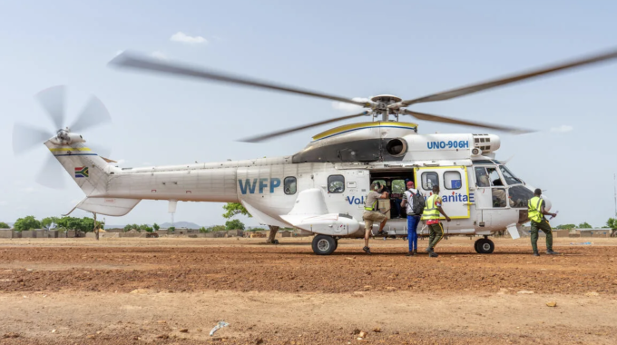 Screenshot 2025-04-03 at 16.01.28.png A WFP helicopter on a dirt field with several people in yellow vests exiting it.