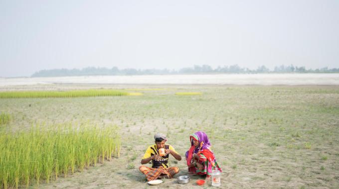 Two individuals sit and eat lunch in a dried floodplain