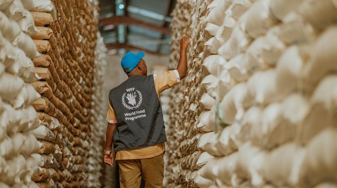 WFP Supply Chain staff walks through row of food parcels.