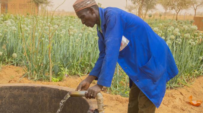 A man accesses water via a well pipe in a field.