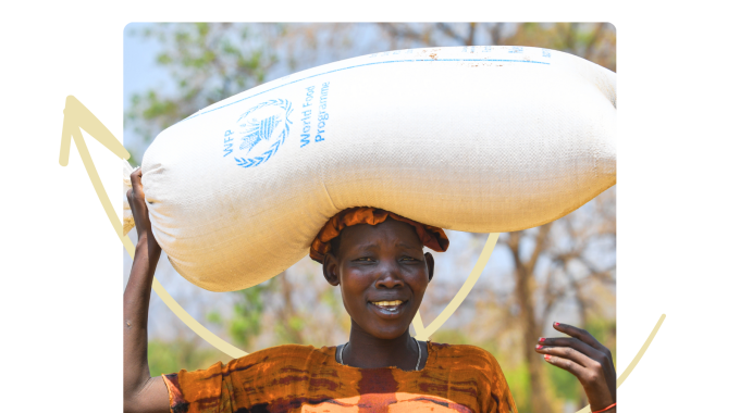 A woman in Ethiopia with a large bag of WFP food on her head, she is smiling towards the camera.