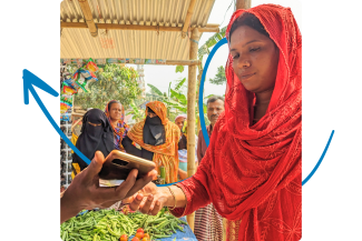 A woman in a red sari is holding a cell phone, looking at the screen with a thoughtful expression.