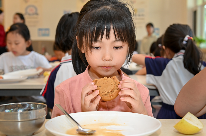 Girl holding up a cookie and looking at a plate; Photo: WFP/Clear Plate
